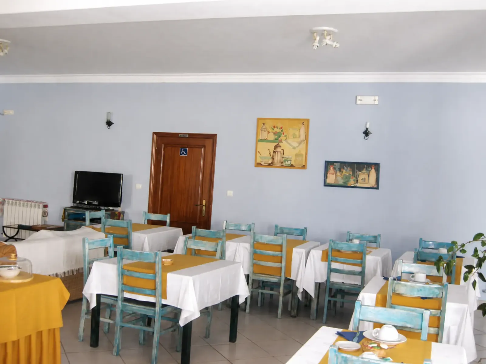 Sala de refeições posta para o pequeno-almoço, com toalhas brancas e cadeiras azuis